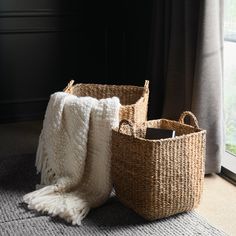 two wicker baskets sitting on the floor next to a window with a white blanket