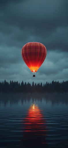 a red hot air balloon flying over a lake at night with the sun reflecting in the water