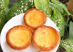 three small pies on a white plate next to green leaves