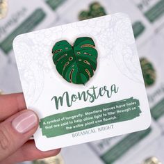 a person holding up a business card with a monstera leaf pin in the middle