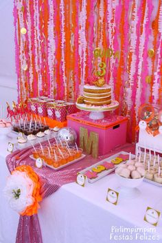 a table topped with cake and cupcakes next to a pink wall covered in streamers