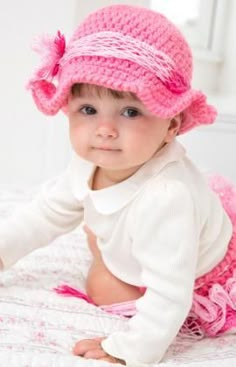 a baby girl wearing a pink hat on top of a bed