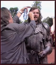 two men dressed in medieval armor, one holding a water bottle and the other fixing his helmet