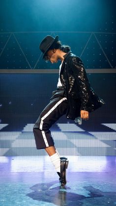 a male in a black jacket and hat is dancing on stage with his legs spread out