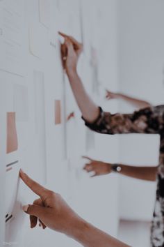 two women pointing at post - it notes on a wall