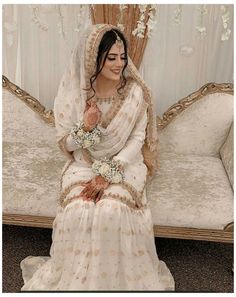 a woman sitting on top of a couch wearing a white dress and holding a bouquet