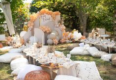 an outdoor party setting with balloons, pillows and table cloths on the grass in front of it