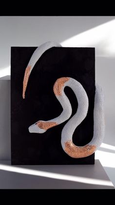 a white and orange snake is on a black square with the letter s in it