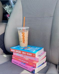 a stack of books sitting on top of a car seat next to a drink