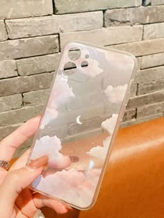 a woman holding up her phone case with clouds on it