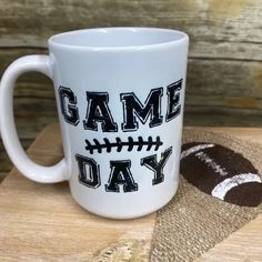 a white coffee mug with the words game day on it sitting next to a football