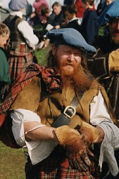 two men in kilts and hats are dressed up for an event with people sitting on the grass behind them