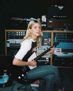 a woman sitting on top of a chair with a guitar in front of an assortment of sound equipment