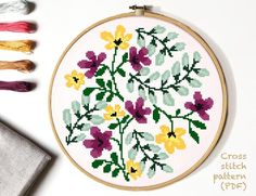 a cross stitch pattern with flowers on it next to some scissors and thread spools