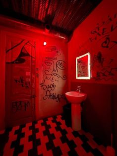 a bathroom with red walls and black and white checkered flooring, graffiti on the wall