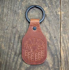 a brown leather keychain with an arrow and pine tree design on the front