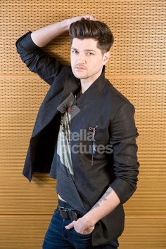 a young man is posing in front of a wall wearing a black jacket and jeans