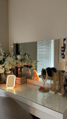 a white desk topped with a mirror next to a vase filled with flowers on top of it