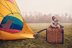 a woman sitting on top of a basket next to a hot air balloon in a field