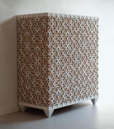 a white cabinet with an intricate design on the front and side panels, sitting against a wall