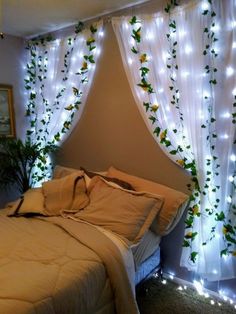 a bed sitting under a window covered in white curtains and lights next to a potted plant