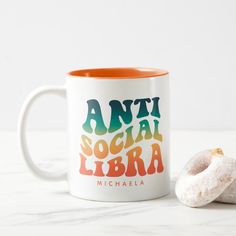 an orange and white coffee mug next to a donut