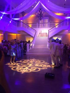 a man and woman standing in front of a crowd at a wedding ceremony with the light projected on the dance floor