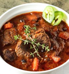 a white bowl filled with beef stew and carrots on top of a marble table