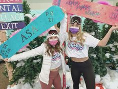 two girls in ski gear hold up signs with words on them and snow covered trees behind them