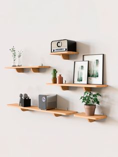 three wooden shelves with pictures, plants and speakers on them against a white painted wall