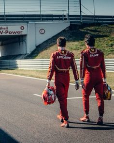 two men in red racing suits walking down a race track