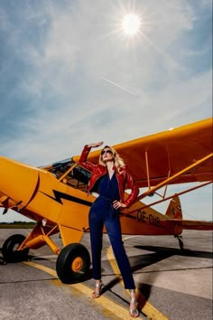 a woman standing in front of an orange plane on the tarmac with sun shining behind her