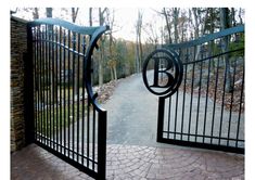 an iron gate opens onto a walkway in front of a stone wall and brick path