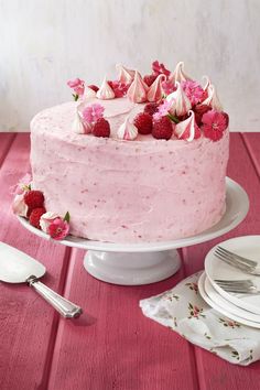 a pink frosted cake with raspberries and flowers on top sitting on a table