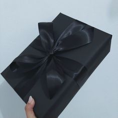 a hand holding a black gift box with a large bow