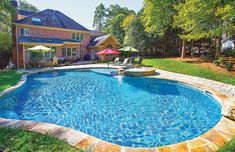 a backyard with a swimming pool surrounded by lawn chairs and umbrellas in the sun