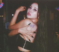 a woman with long dark hair and tattoos on her chest posing for a photo in front of a neon sign