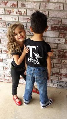 two young children standing next to each other in front of a brick wall with the words t birds on it