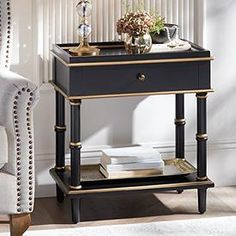 a black and gold side table with flowers on it next to a white chair in a living room