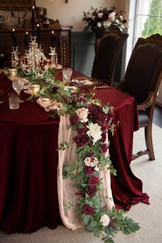 the table is set with red and white flowers, greenery and candles on it