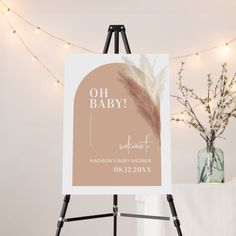 a baby shower sign on an easel next to a vase with flowers in it