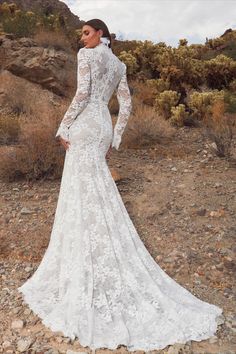 a woman standing in the desert wearing a wedding dress with long sleeves and an open back