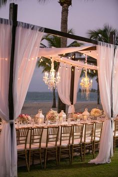 an outdoor dining area with white drapes and chandeliers