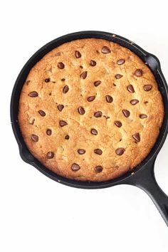 a chocolate chip cookie in a cast iron skillet on a white table with a spoon