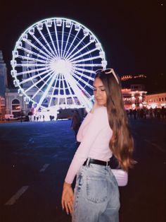 a woman standing in front of a ferris wheel at night with her long hair pulled back