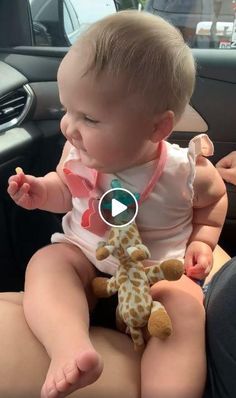 a baby sitting in the back seat of a car holding a stuffed giraffe