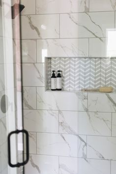 a bathroom with white marble and black handles on the shower door, along with two bottles of hand soaps