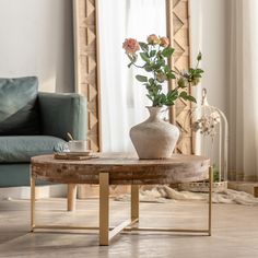 a vase with flowers on a table in front of a couch and mirror, next to a coffee table