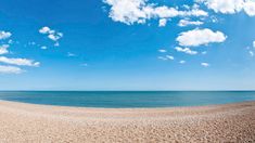 a sandy beach with blue sky and white clouds