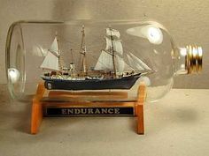 a model ship in a glass bottle on a wooden base with a sign underneath it